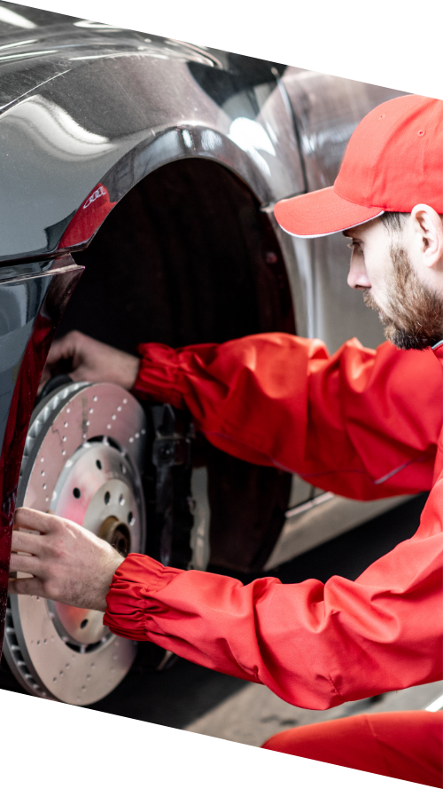 A man in a red jacket repairs the brake of a car, focused on ensuring its proper function.